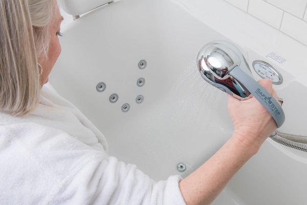 woman using a handheld shower wand in her walk-in tub