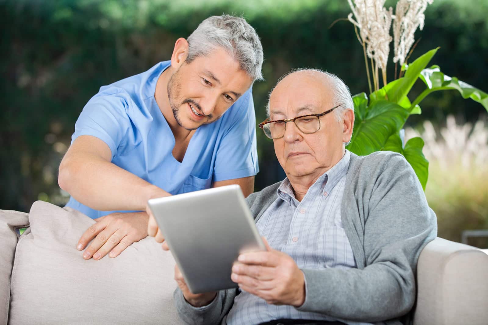 caregiver helping elderly man research walk-in tubs on his tablet
